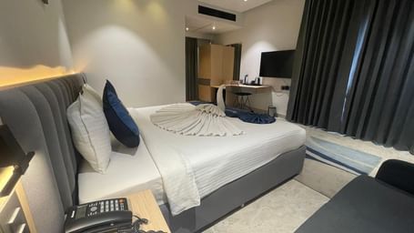 Bedroom at Hotel Kyzen HiTech City with a king bed, side table and curtained windows.